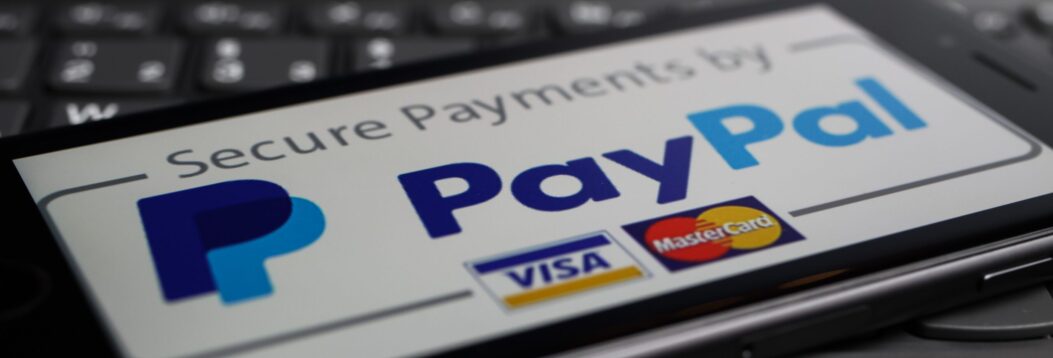 A smartphone screen displays the PayPal logo with Visa and MasterCard logos, indicating secure payment options, placed on a laptop keyboard.